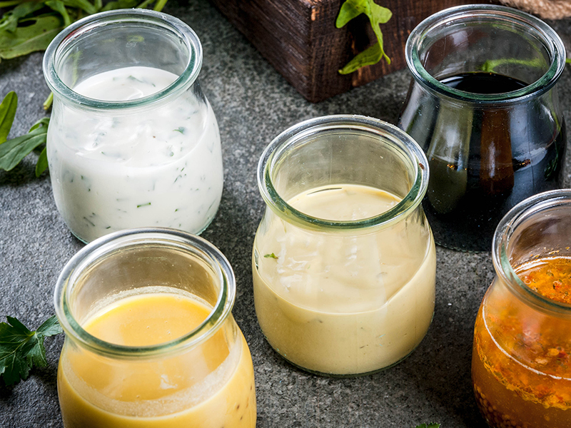 Two salad dressings in jars beside fresh greens